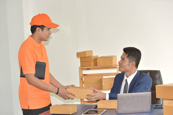 Teslimat hizmeti konsepti, turuncu üniformalı genç Asyalı işçilerin iş adamlarına paket teslimatı.. - Fotoğraf, Görsel