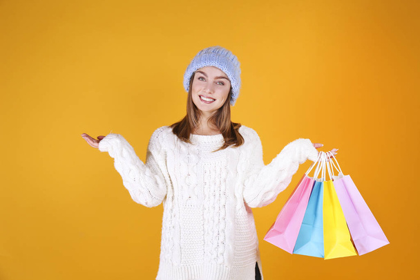 Close up portrait of a young beautiful woman with light make up on, wearing knitted sweater & blue woolen beanie. Attractive female in winter knitwear outfit, isolated on yellow background. Copy space - Photo, image