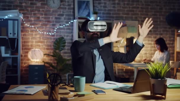 Man using virtual reality glasses moving arms sitting at desk in dark office - Metraje, vídeo
