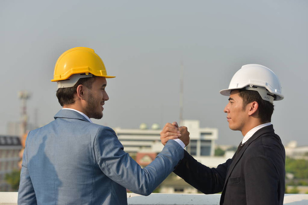 Üzletemberek kemény kalapban, együtt dolgoznak, kezet ráznak a város hátterére.. - Fotó, kép
