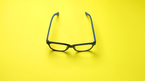 Menselijke handen zoeken, vinden en nemen bril in blauw plastic frame. Op gele achtergrond. - Video