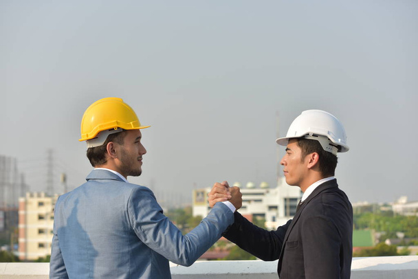Üzletemberek kemény kalapban, együtt dolgoznak, kezet ráznak a város hátterére.. - Fotó, kép
