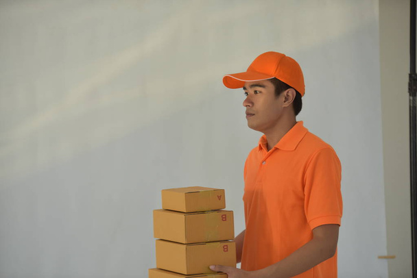 Fiatal ázsiai munkavállaló narancssárga szállítási szolgáltatás egyenruha holding csomagok - Fotó, kép
