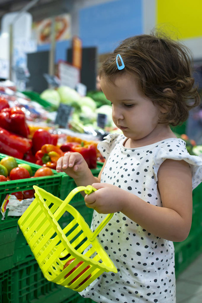 Девочка покупает помидоры в супермаркете. Ребенок держит маленький барельеф
 - Фото, изображение