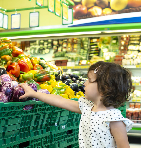 Child shopping eggplants in supermarket. Concept for buying frui - Фото, изображение