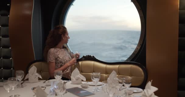 Mulher assistindo por do sol da janela no navio de cruzeiro de luxo com um copo de vinho em restorante
. - Filmagem, Vídeo