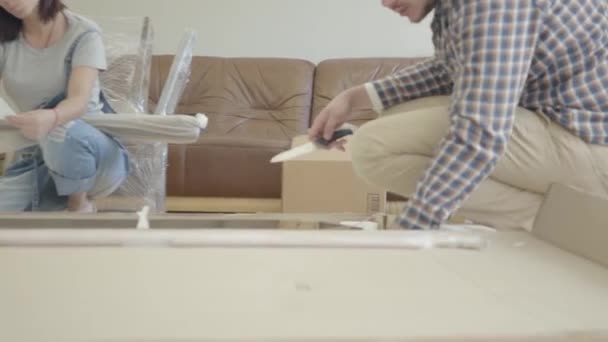 Young Caucasian family unpacking parcel in the living room. Happy couple furnishing their new house. Start of future life. Moving in. - Materiał filmowy, wideo