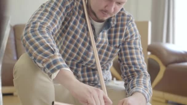 Young handsome Caucasian man assembling new furniture in the living room. Happy family furnishing their new house. Start of future life. Moving in. - Footage, Video