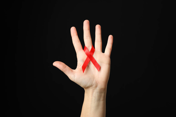 Hand and red awareness ribbon against black background, space fo - Photo, image