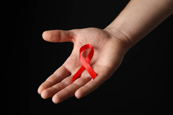 Hand and red awareness ribbon against black background, space fo - Photo, Image