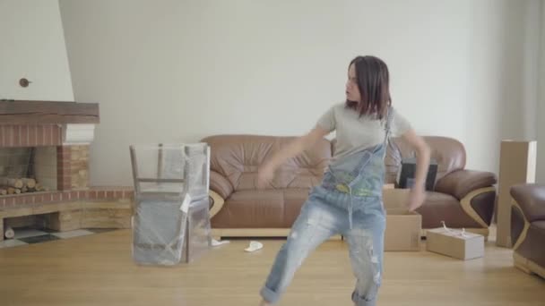 Young cheerful Caucasian woman dancing in the living room with unpacked furniture. Happy girl moving in new house. New life, future. - Кадри, відео