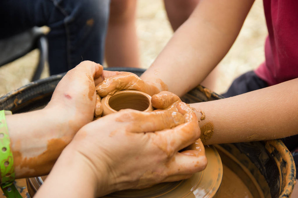 Una vista de cerca sobre el proceso de producción de cerámica en la rueda del alfarero con los niños. Artesanía de arcilla con concepto de niños
. - Foto, Imagen