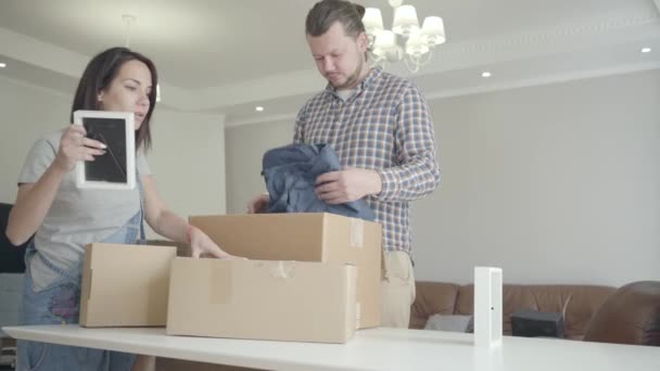 Happy young couple unpacking their belongings in new house. Positive Caucasian family standing in living room with cardboard boxes. Soulmates moving in new home. - Video