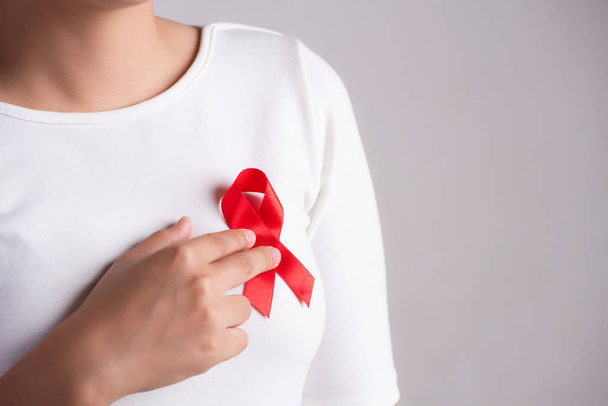 Primer plano de la cinta roja de la insignia en el pecho de la mujer para apoyar el Día del SIDA. Concepto de concienciación sobre salud, medicina y sida. - Foto, Imagen