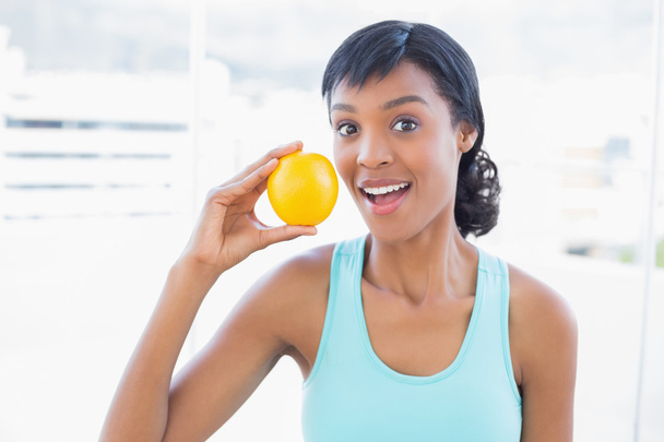 Surprised black haired woman holding an orange - Foto, Imagen