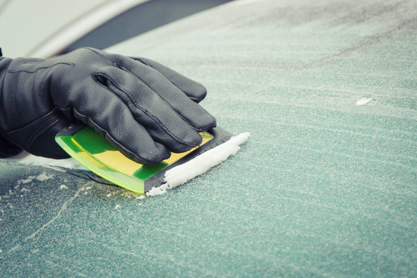 Hand of man using scraper to remove ice from window in car, winter problems - Zdjęcie, obraz