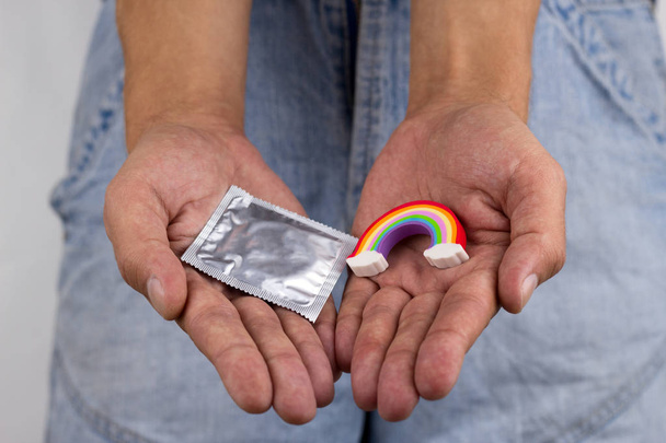 man holding a rainbow trinket and a condom pack , close up of male hands - Valokuva, kuva