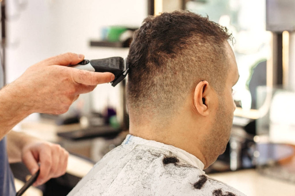Fryzjer podejmowania stylowe fryzury z profesjonalną maszyną w salonie fryzjerskim. Fryzura dla Tureckiego mężczyzny - Zdjęcie, obraz