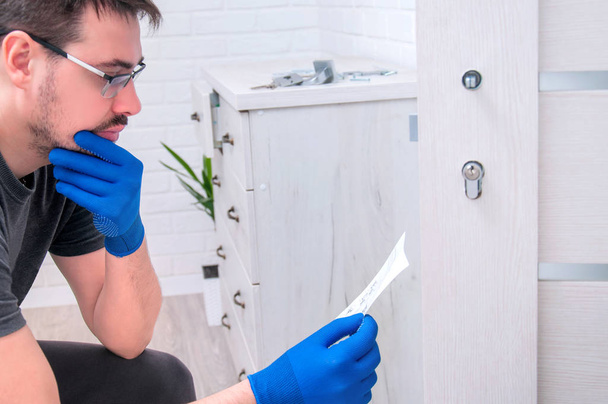 The guy installs new handles and a lock for the door to the room. Repair in the house. A guy in blue gloves holds an instruction in his hands and reads it. Installing a door lock. - Photo, Image