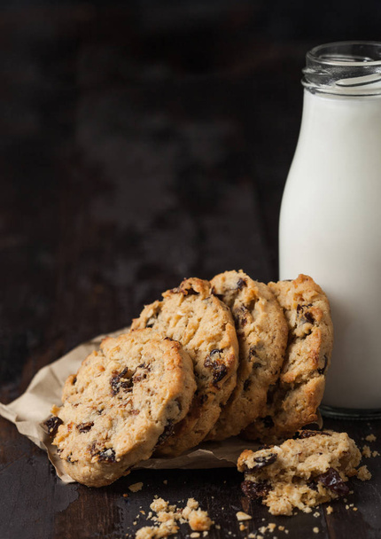 Homemade organic oatmeal cookies with raisins and apricots and bottle of milk on dark wooden background. - Foto, Bild