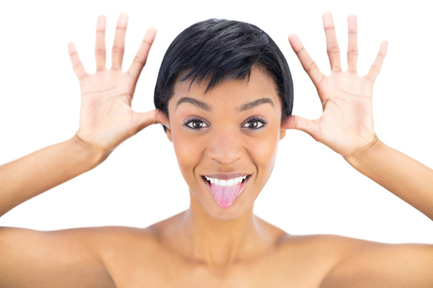 Joyful black haired woman posing with tongue out and hands around her head - 写真・画像