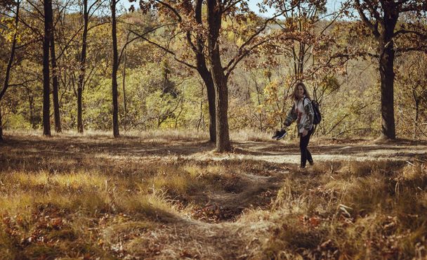 Krásná mladá dívka kráčí bosá s tenisky v ruce do lesa. Je slunečný podzimní den se žlutými listy a suchou trávou. Fotografie s výběrovým zaměřením - Fotografie, Obrázek