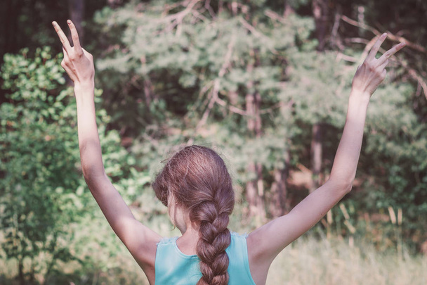 widok z tyłu dziewczyny z długimi włosami w warkoczu, wskazując dwa palce w górę gest, wolna przestrzeń. Wolność, spokój ducha koncepcja wellness. - Zdjęcie, obraz