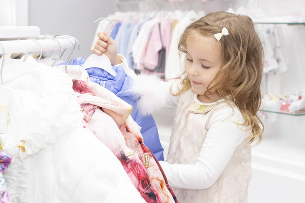 shopping. discounts. little girl shopaholic. girl delighted with beautiful jackets, chooses warm clothes. shopping center, shopping. emotions - 写真・画像