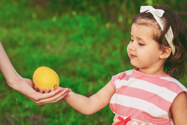 Egy kislány mosolyog és átad egy friss citromot, mint vitaminforrást egy másik női kéznek, zöld alapon. - Fotó, kép