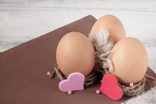 Three Easter eggs with feathers and hearts are in decorative nests. White and brown wooden background. The large pal. Festive card - Foto, Imagem