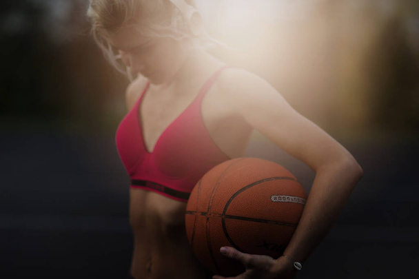 Portrait of a gorgeous concentrated beautiful strong athletic woman outdoors posing while listening to music with headphones holding a basketball.healthy lifestyle concept, sporty girl - Foto, immagini