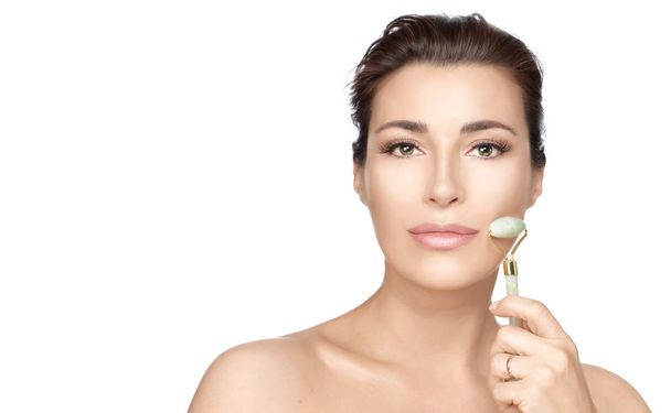 Woman with healthy fresh skin using jade face roller in a skinca - Photo, Image