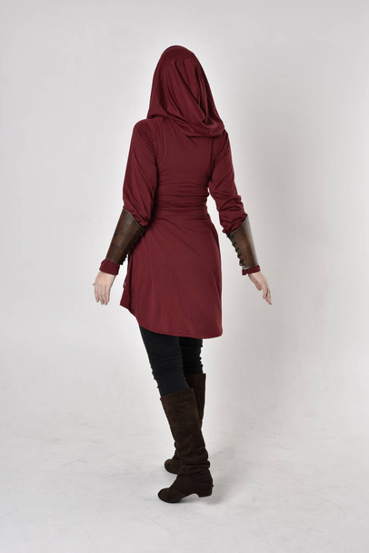 full length portrait of a girl wearing fantasy long red hooded tunic. standing pose with back to the camera. - Photo, Image