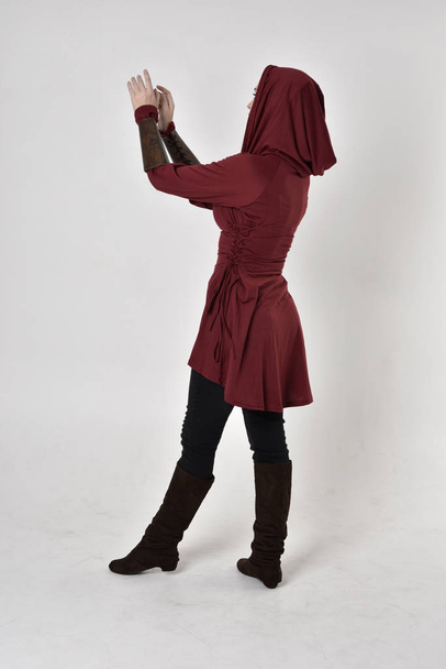 ολόσωμο πορτρέτο ενός κοριτσιού που φορούσε φανταστικό μακρύ κόκκινο χιτώνα με κουκούλα. όρθια στάση με την πλάτη στην κάμερα. - Φωτογραφία, εικόνα