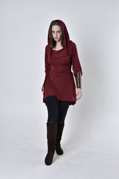 full length portrait of a brunette girl wearing a red fantasy tunic with hood. Standing pose on a white studio background. - Photo, Image