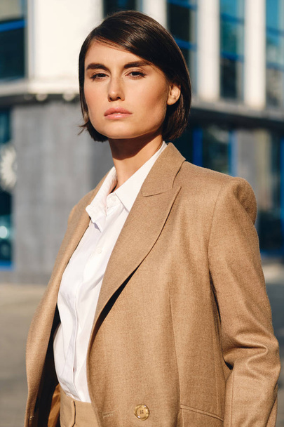 Young attractive stylish businesswoman in suit intently looking in camera on street - Фото, изображение