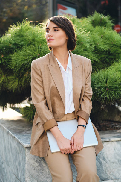 Jeune femme d'affaires élégante attrayante en costume beige avec ordinateur portable Dreamily côté extérieur
 - Photo, image