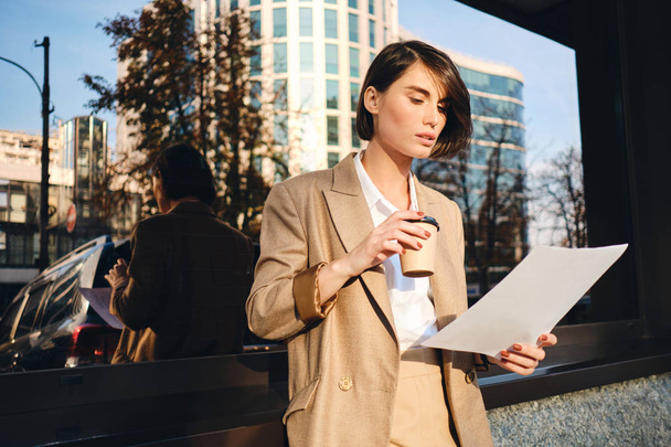 Young confident stylish businesswoman with coffee to go working on street - Photo, Image