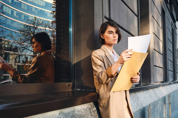 Young confident stylish businesswoman thoughtfully working with papers outdoor - Photo, Image