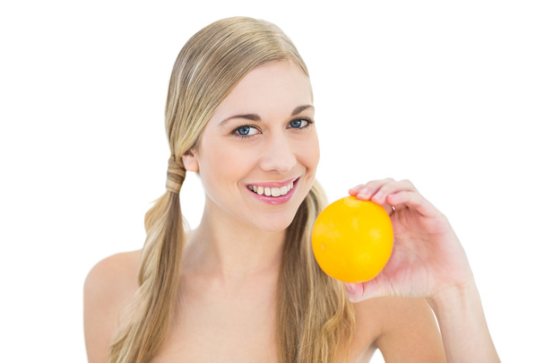 Smiling young blonde woman holding an orange - Foto, Bild