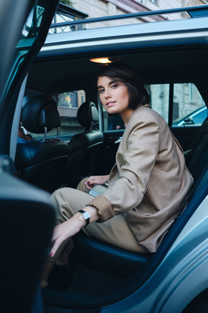 Young attractive stylish businesswoman sitting in car dreamily looking in camera  - Фото, изображение