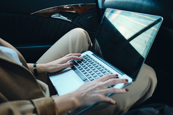 close-up stijlvolle zakenvrouw werken op laptop in auto - Foto, afbeelding