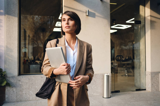 junge attraktive stilvolle Geschäftsfrau mit Laptop schaut verträumt auf der Straße weg - Foto, Bild