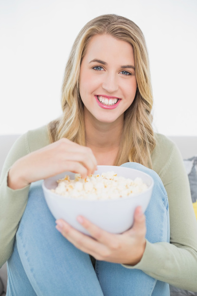 Cheerful pretty blonde eating popcorn sitting on cosy sofa - Foto, Bild