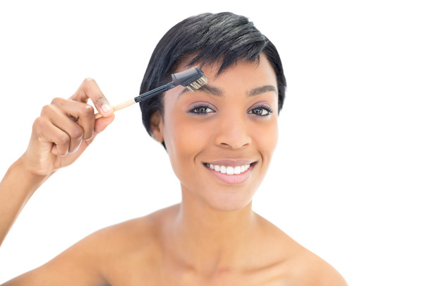 Happy black haired woman brushing her eyebrows - Foto, afbeelding