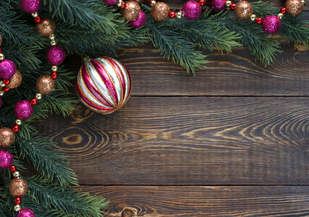 Frame of fir branches, pink and orange Christmas tree balls on wooden brown background.  - Foto, imagen