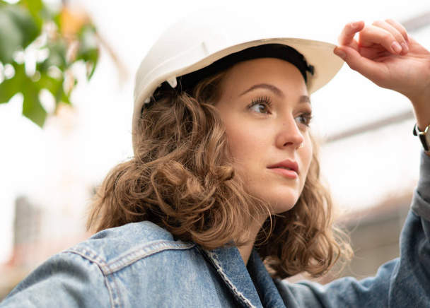 Close up retrato de uma fábrica pensativa e contemplativa empregada feminina vestindo um chapéu duro de proteção branca
 - Foto, Imagem