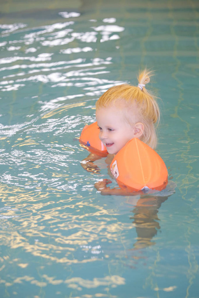 Yüzme havuzunda yürüyen çocuk turuncu şişme bebek yüzme yüzüğü takıyor. - Fotoğraf, Görsel