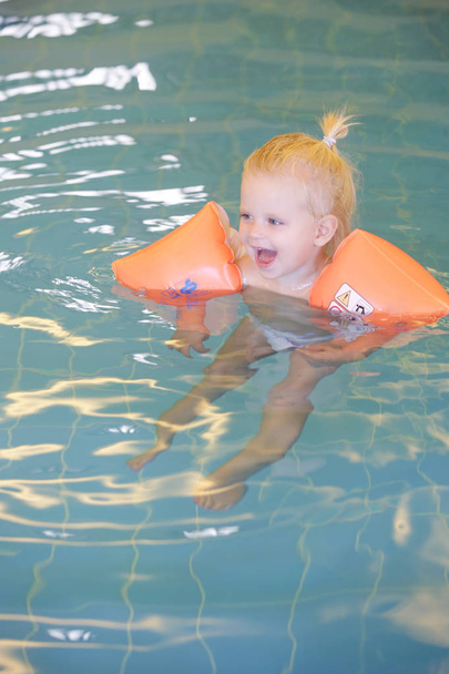 Βρέφος στην πισίνα φορώντας πορτοκαλί φουσκωτό δαχτυλίδι μωρό κολύμπι - Φωτογραφία, εικόνα