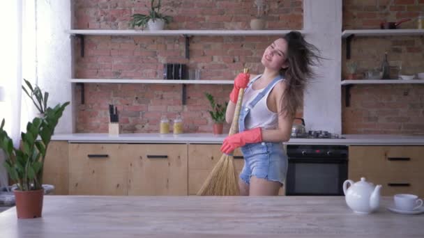 Home routines, joyful housekeeper woman dancing and sings in besom like microphone during household duties - Materiał filmowy, wideo